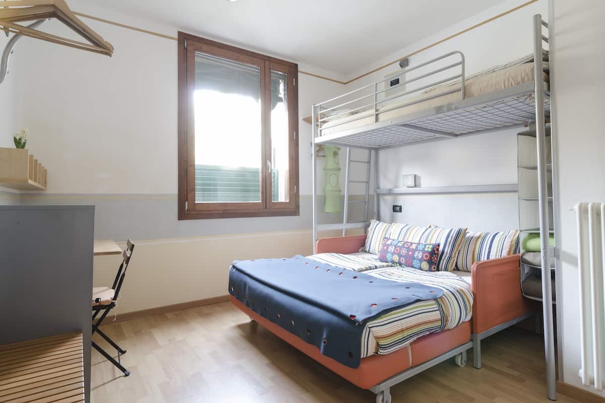 Een slaapkamer met een stapelbed, bureau en stoel, een raam en een radiator.
