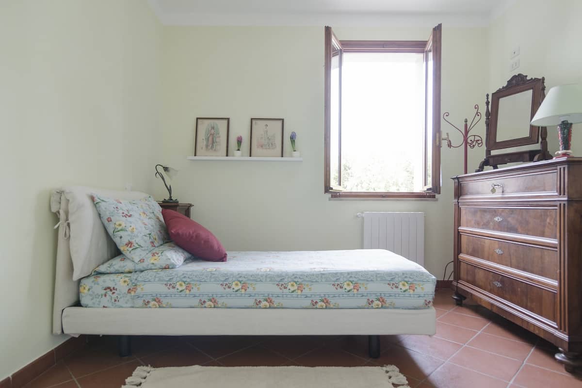 Een slaapkamer met een bed, een dressoir, een raam en wandplanken met foto's.