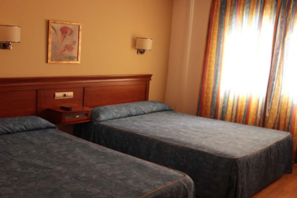 A hotel room with two single beds, a wooden headboard, bedside tables, and a painting on the wall.