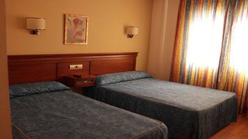 A hotel room with two single beds, a wooden headboard, bedside tables, and a painting on the wall.