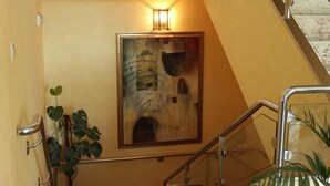 A staircase with a handrail, a wall-mounted light fixture, and a framed artwork depicting a building facade. - Hostal Tio Pepe II (Bembibre)