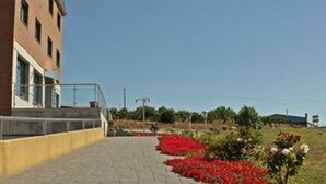 A building with a yellow exterior and a paved walkway leading to a gated entrance. - Hostal Tio Pepe II (Bembibre)