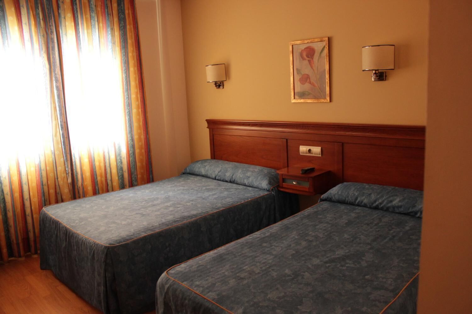 Una habitación de hotel con dos camas individuales, un cabecero de madera, una mesita de noche y un cuadro en la pared.