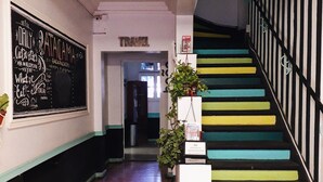 A hallway with a blackboard on the left, a staircase with colorful steps, and a plant in the center. - Atacama Backpackers (Santiago)