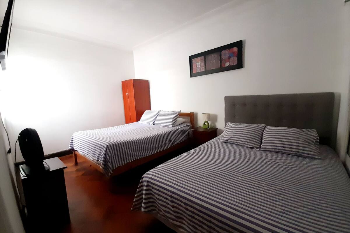 A hotel room with two beds, a wardrobe, a desk, and a wall-mounted picture.