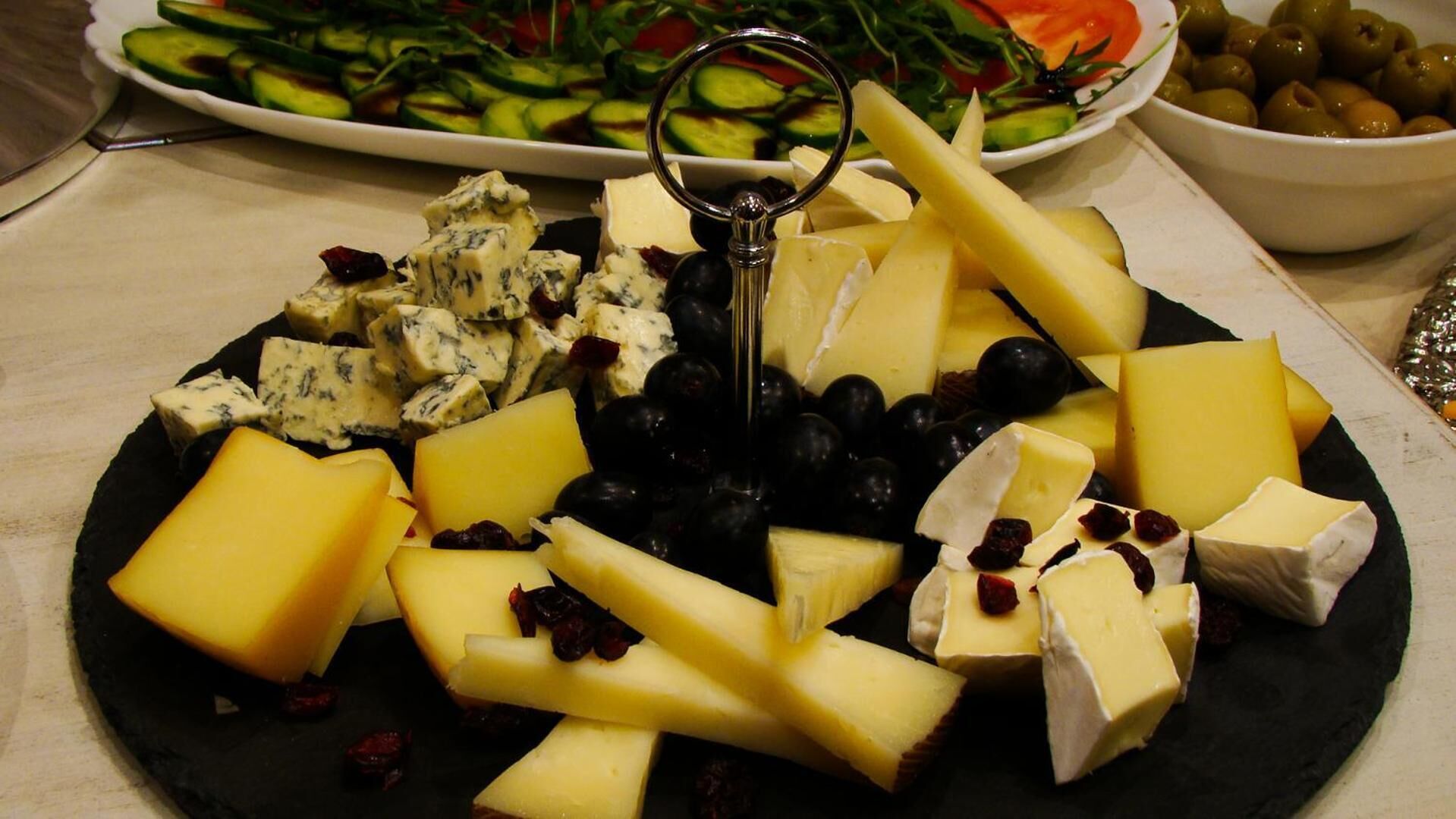 A platter of assorted cheeses, grapes, and dried fruits on a black plate.