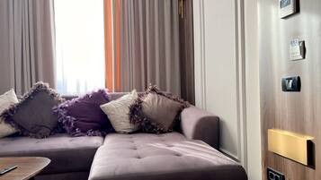 A modern living room with a sectional sofa, a small wooden table, and a wall-mounted thermostat.