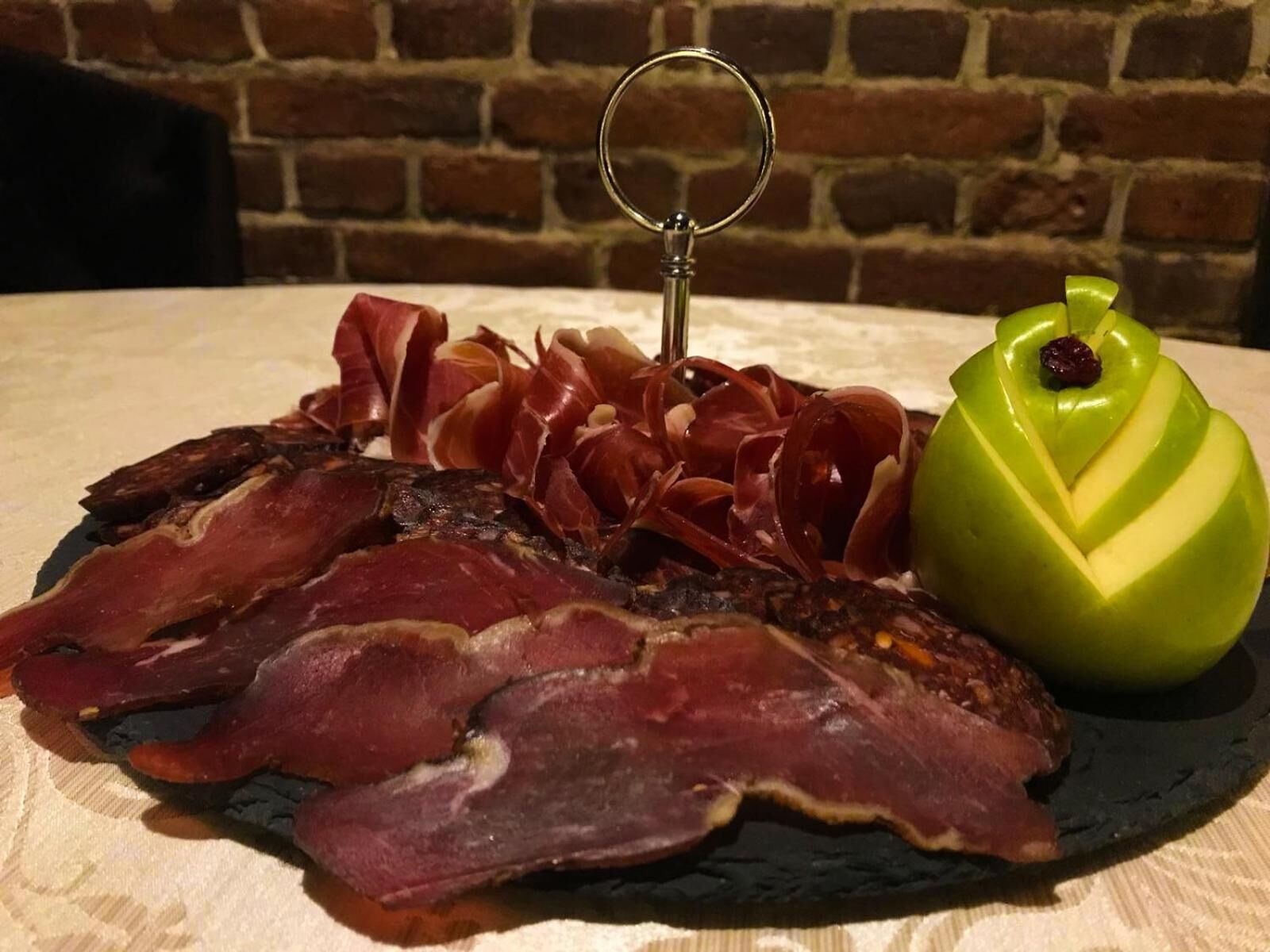 A charcuterie board with sliced meats and a carved apple on a slate plate.