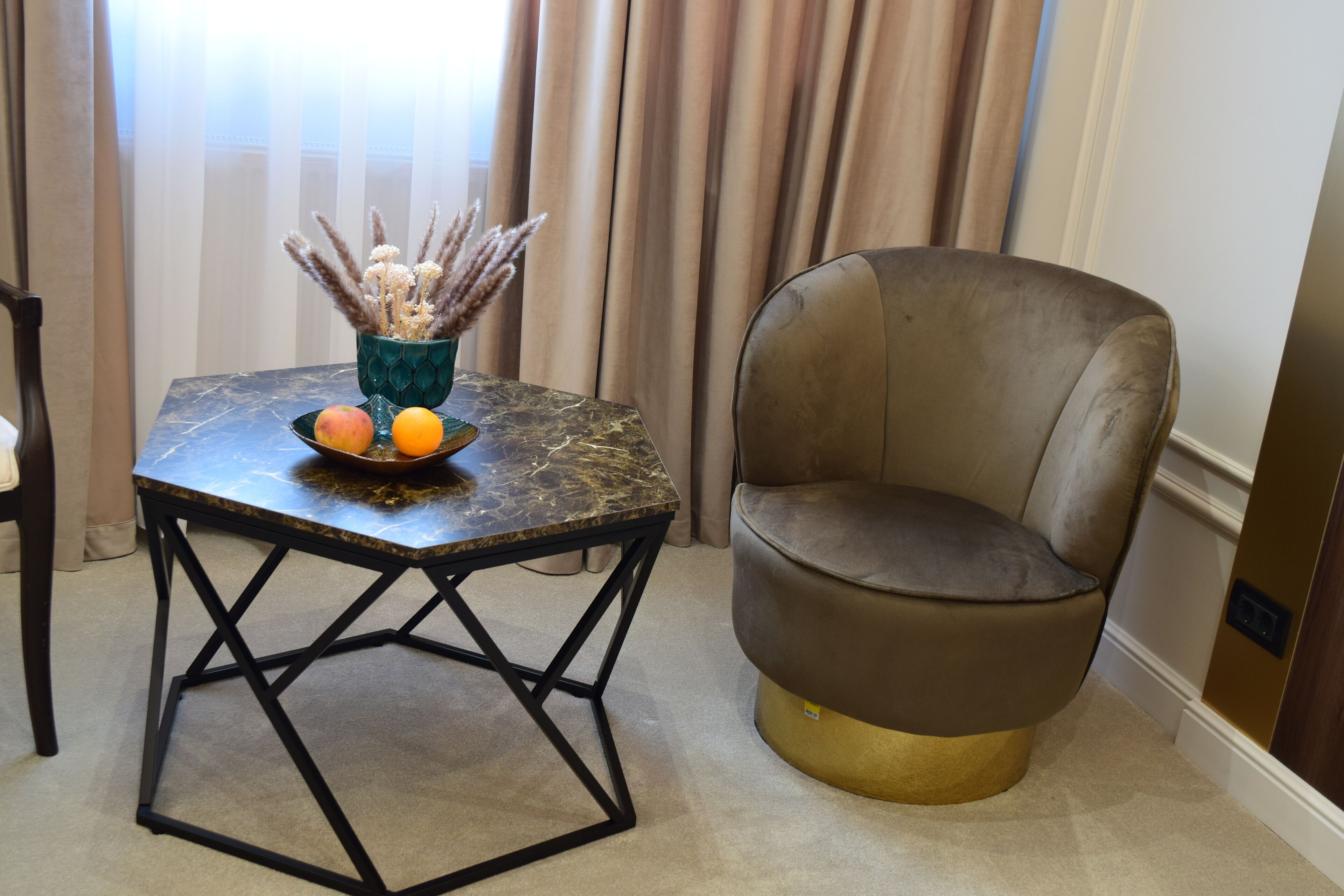 Una habitación moderna con una mesa de mármol, un florero con plantas secas y un sillón mullido.