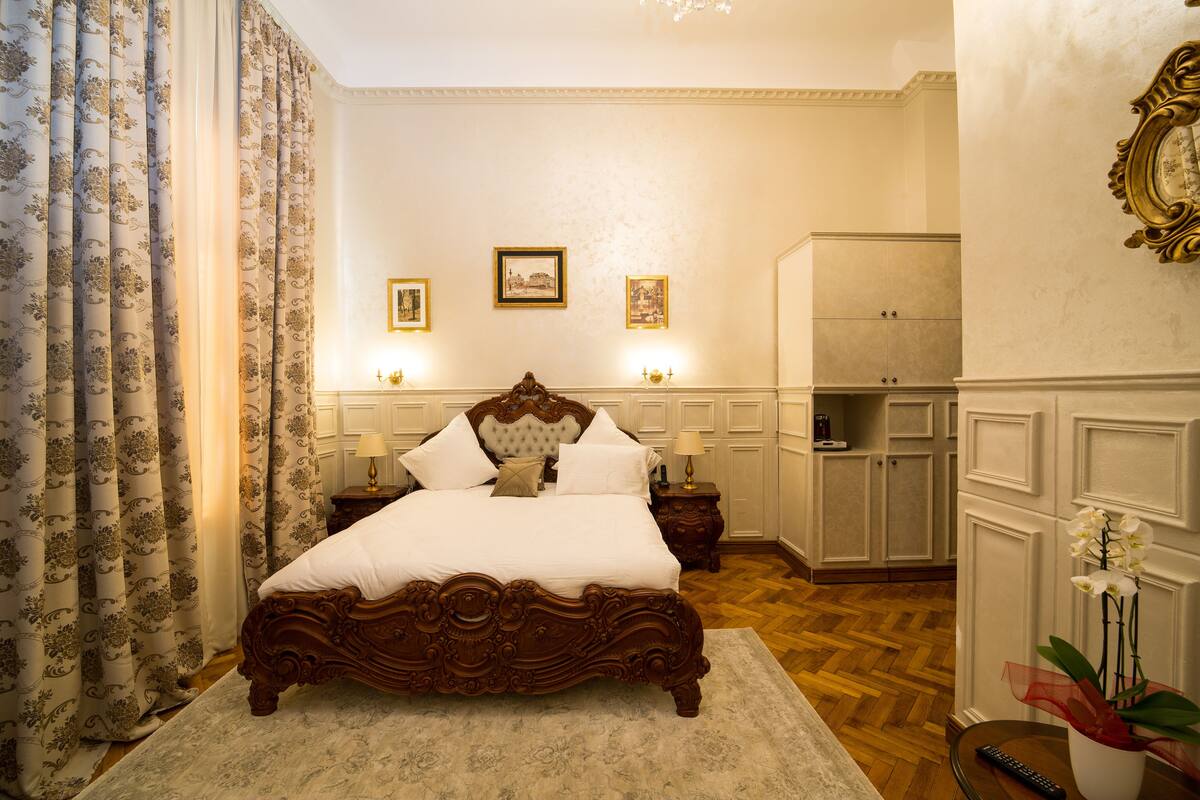 A bedroom with a large bed, a wardrobe, and a nightstand with a lamp.