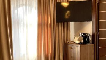 Ein Hotelzimmer mit großem Fenster, einem flachbildfernseher an der Wand, einem Holzschrank und einem Glastisch mit einer Tasse.