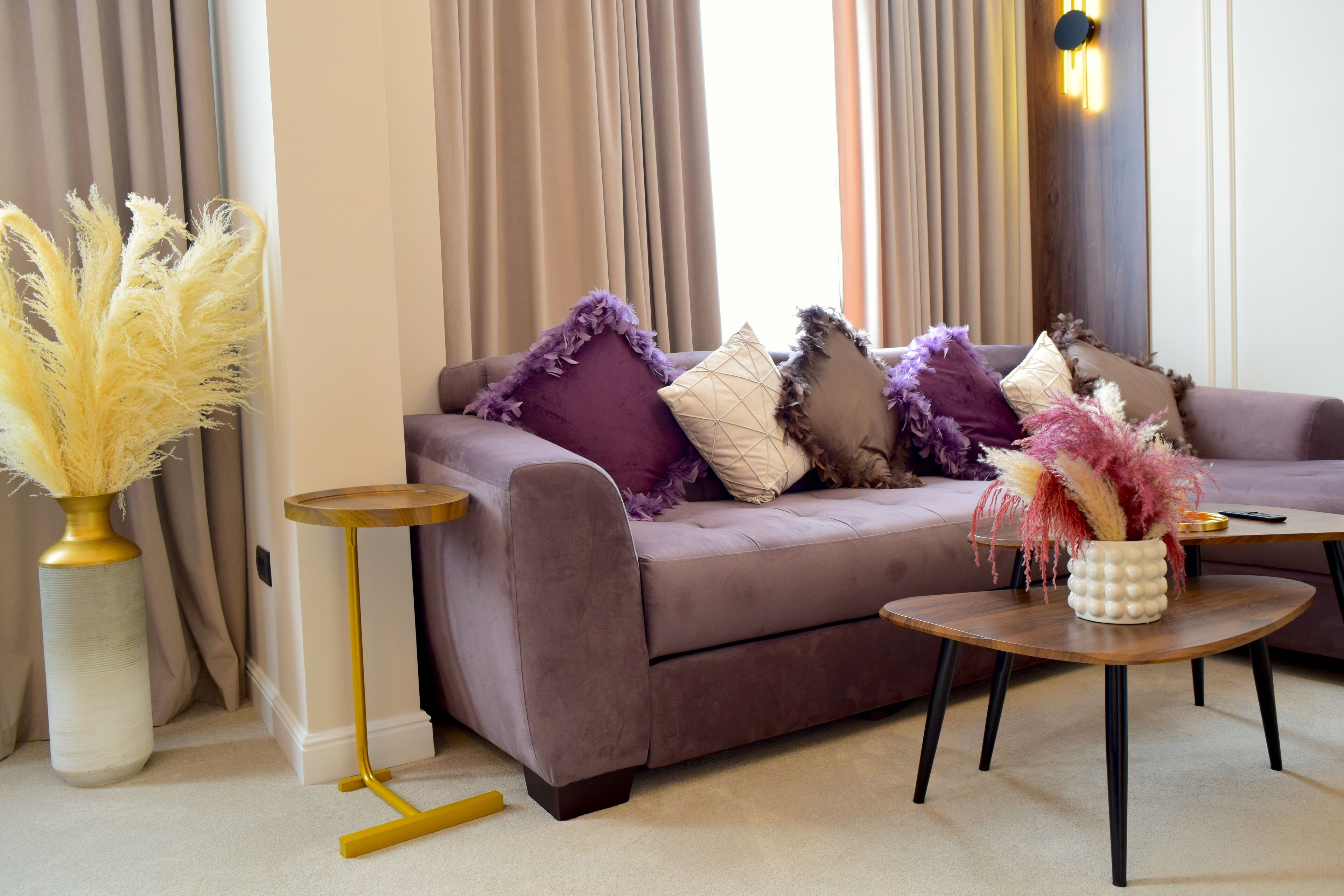 A modern living room with a sofa, decorative pillows, a round coffee table, and a vase with dried plants.