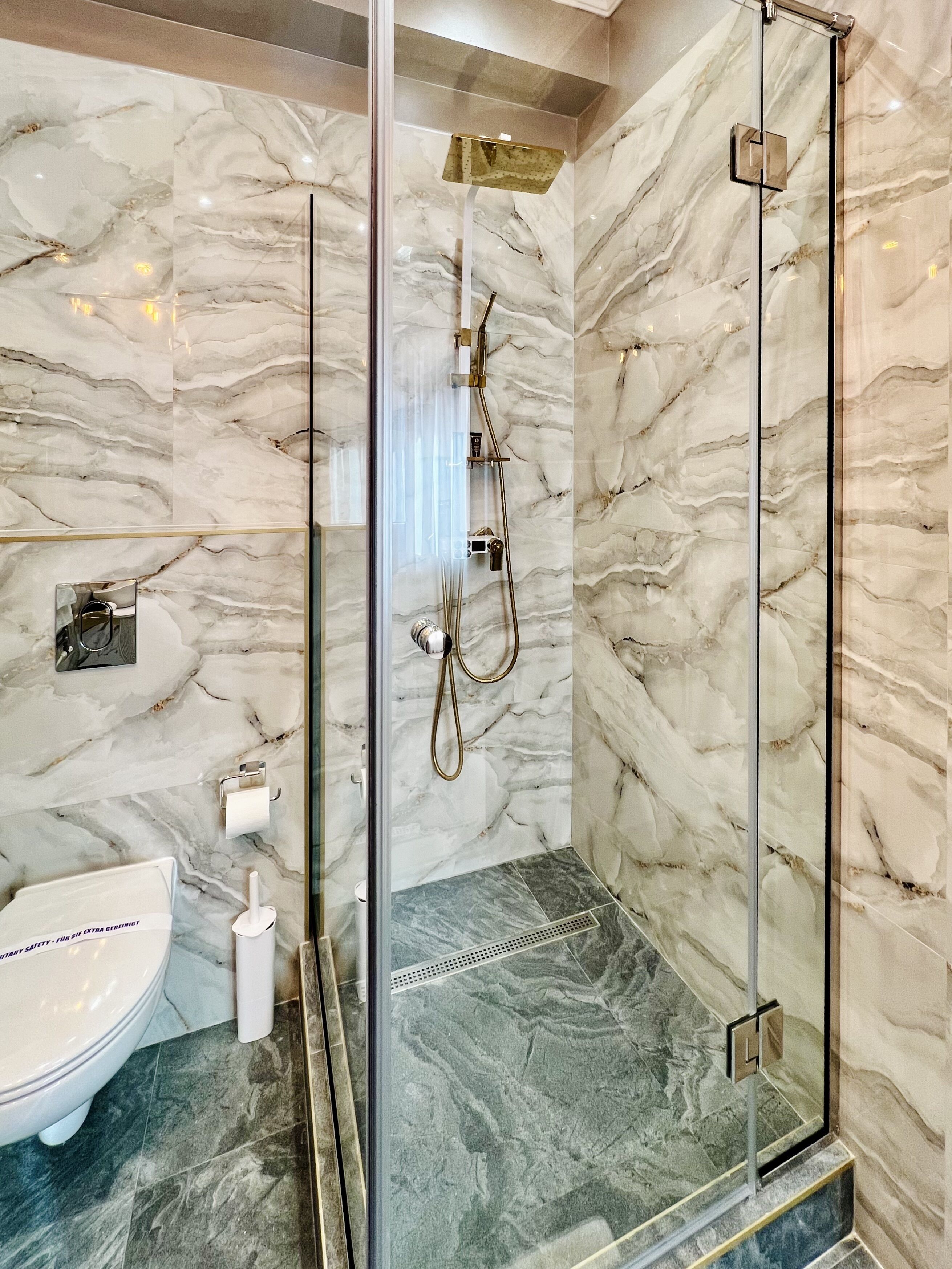Een moderne badkamer met een douchecabine van glas, marmeren wanden en een toilet.