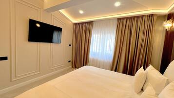 A hotel room with a large bed, a flat-screen TV mounted on the wall, and a window with curtains.