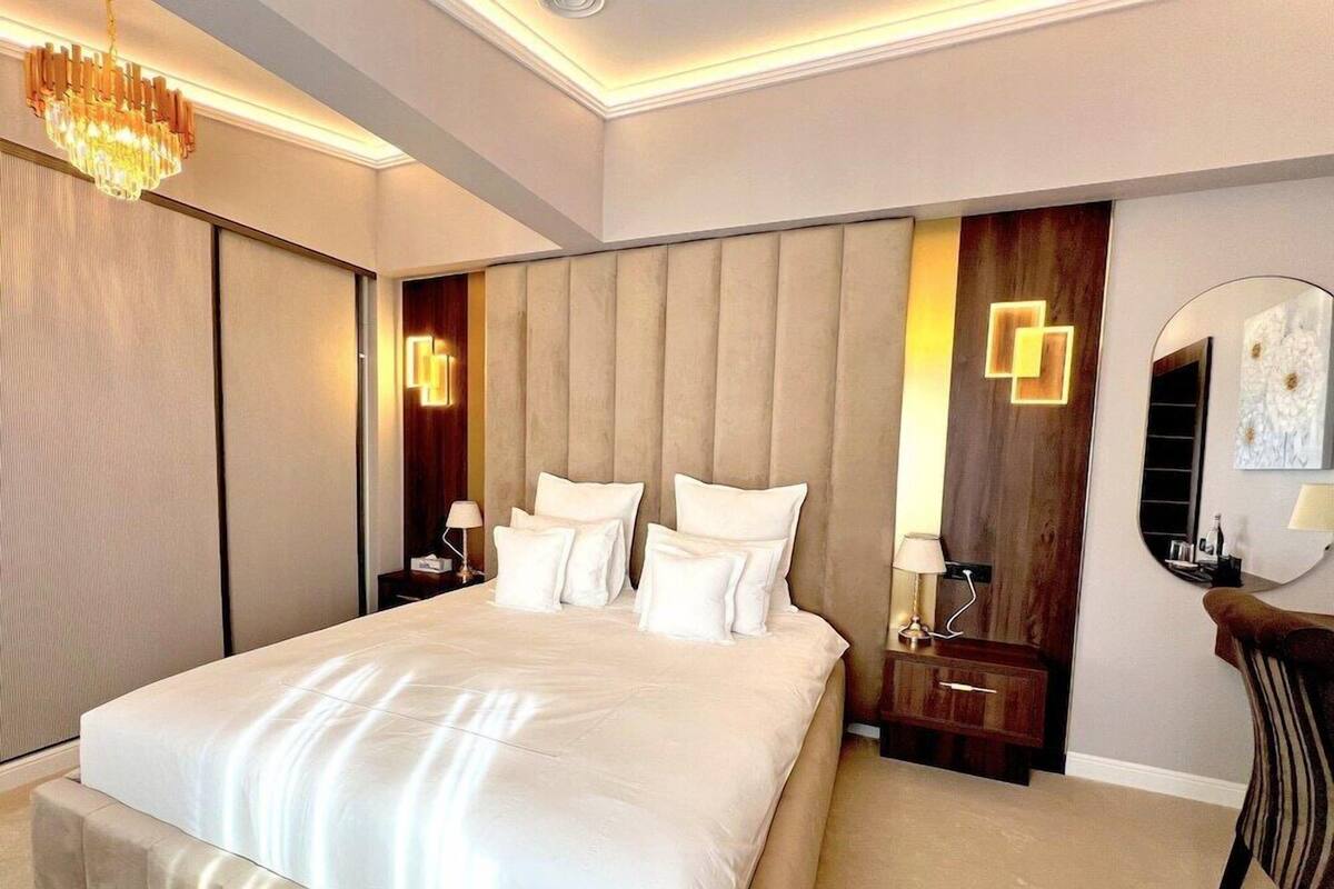 A modern hotel room with a large bed, a round mirror, and a chandelier.
