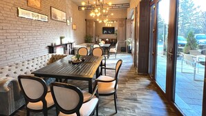 A dining area with a brick wall, a wooden table, and chairs. There is a sofa and a television on the wall. - Hotel Boutique 5 Continents (Craiova)