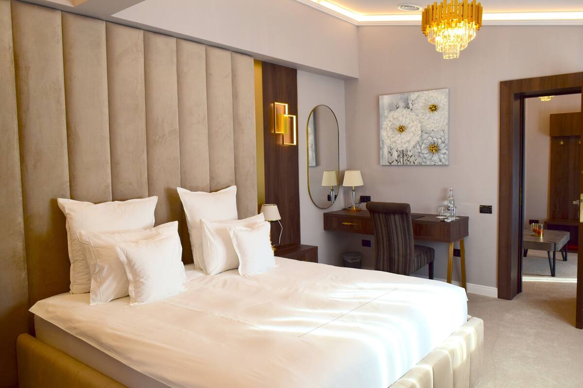 A hotel room with a large bed, a desk, a chair, and a mirror.