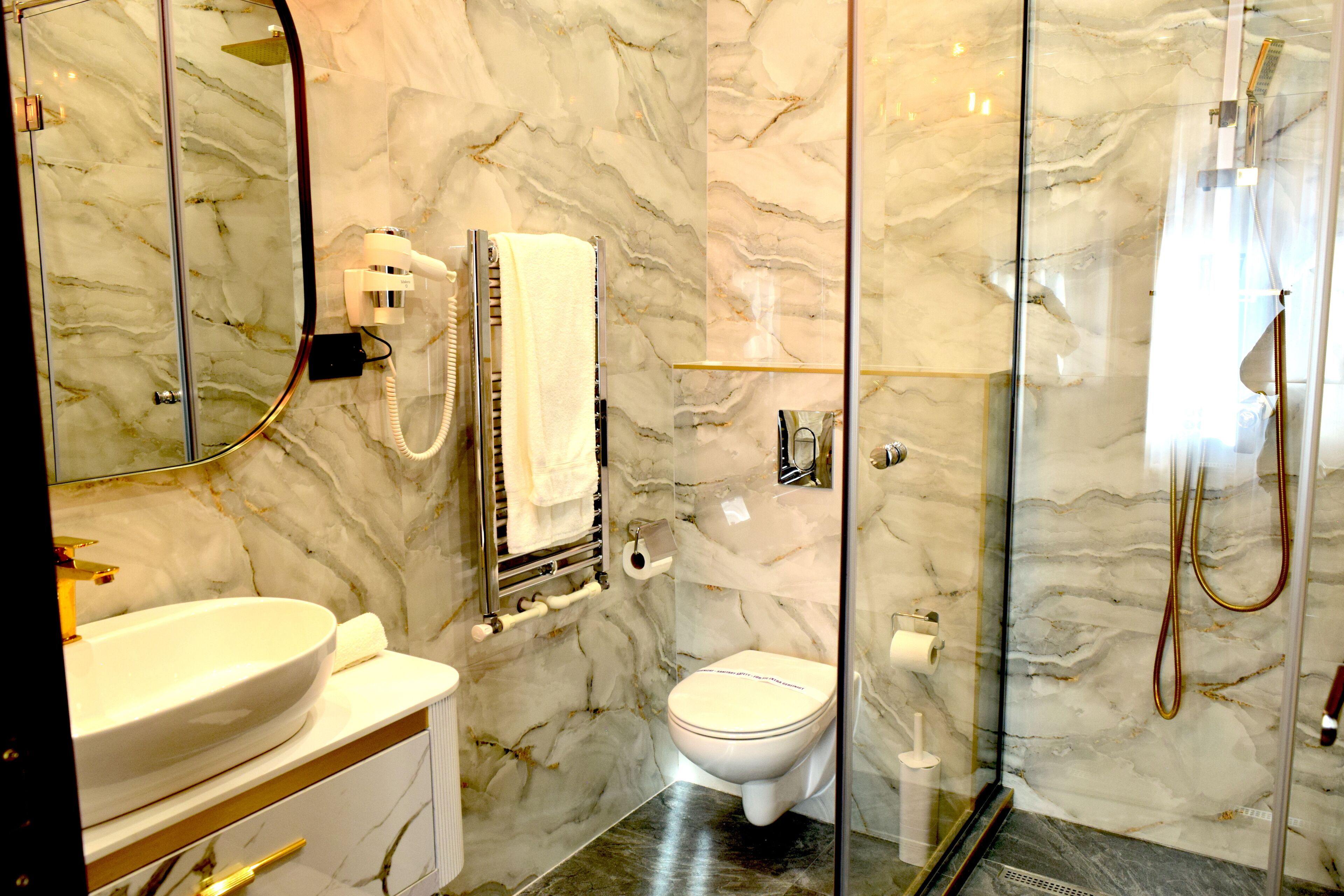 Une salle de bain avec un mur en marbre, un lavabo blanc, des toilettes et une douche séparée par une paroi de verre.