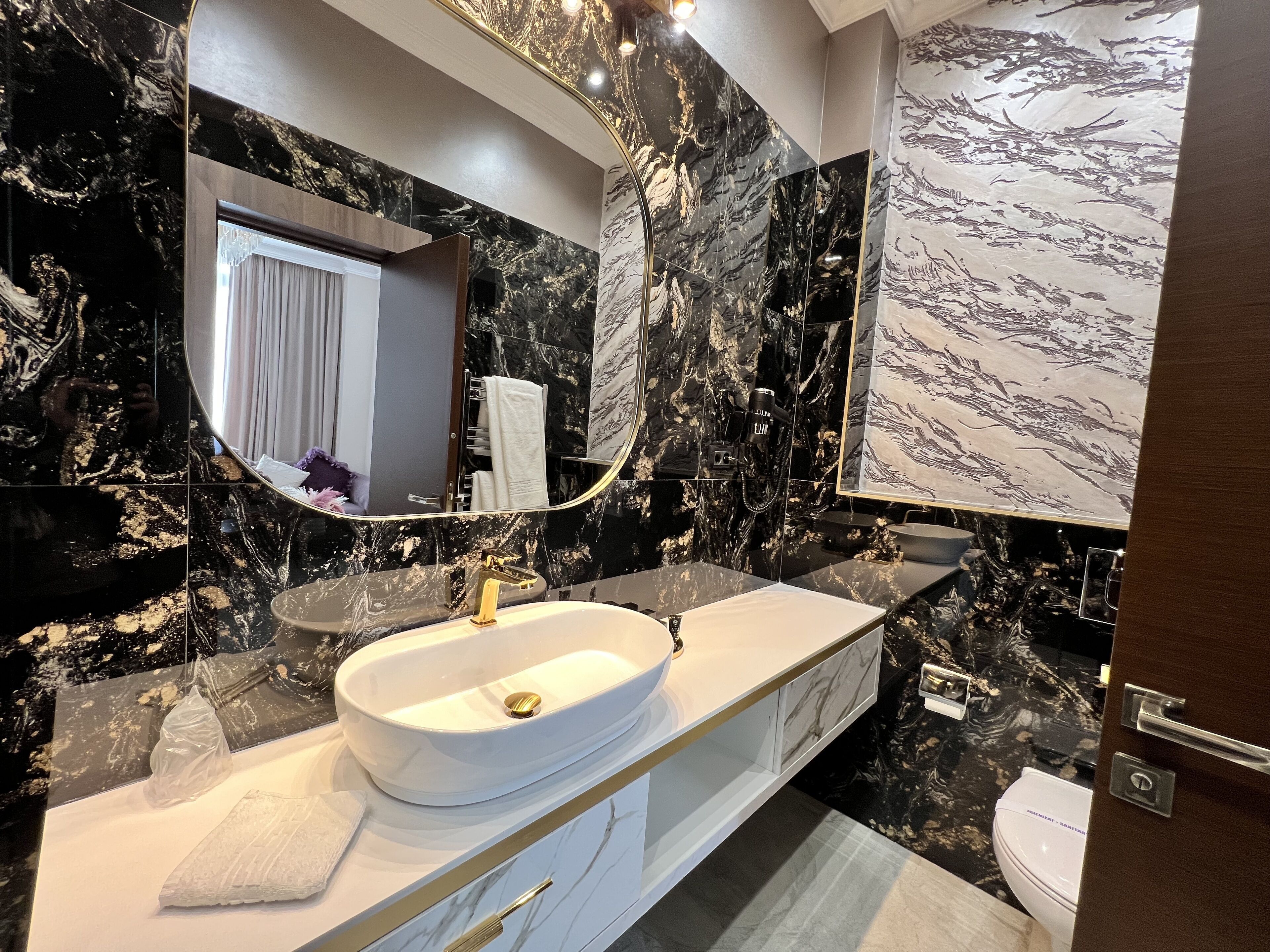 A modern bathroom with a white sink, gold faucet, and marble walls.