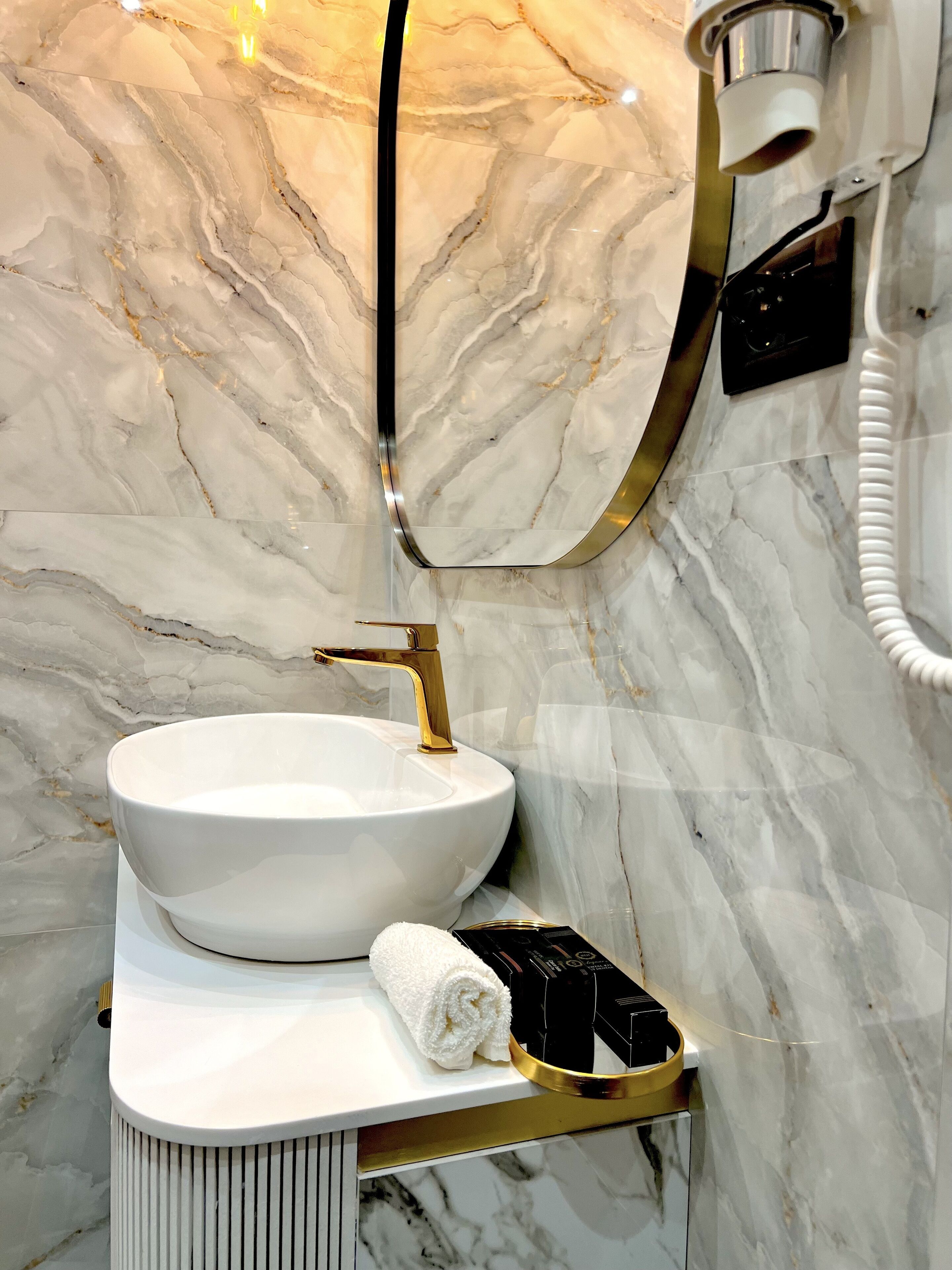 A bathroom with a white marble sink, gold faucet, and a towel on a white countertop.