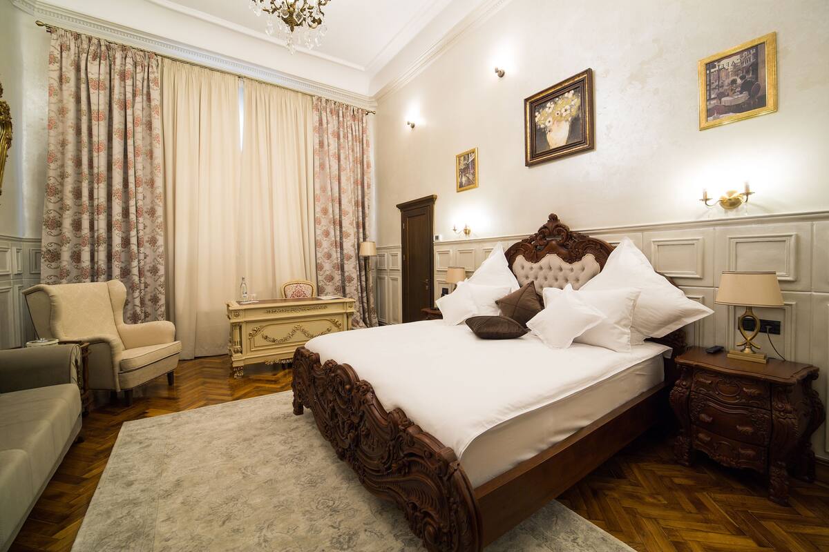 A classic bedroom with a large bed, a chair, a dresser, and a chandelier.