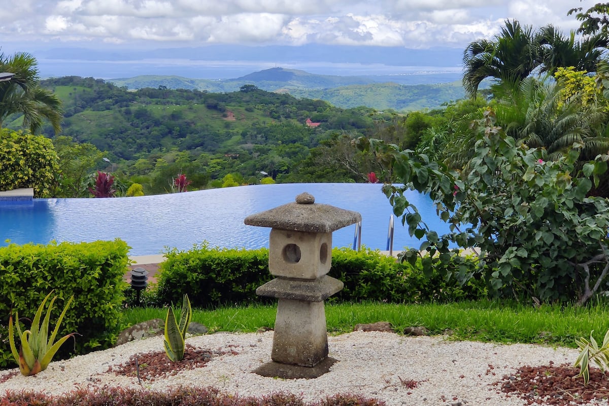 Un farol de piedra, un estanque y abundante vegetación con una vista distante.