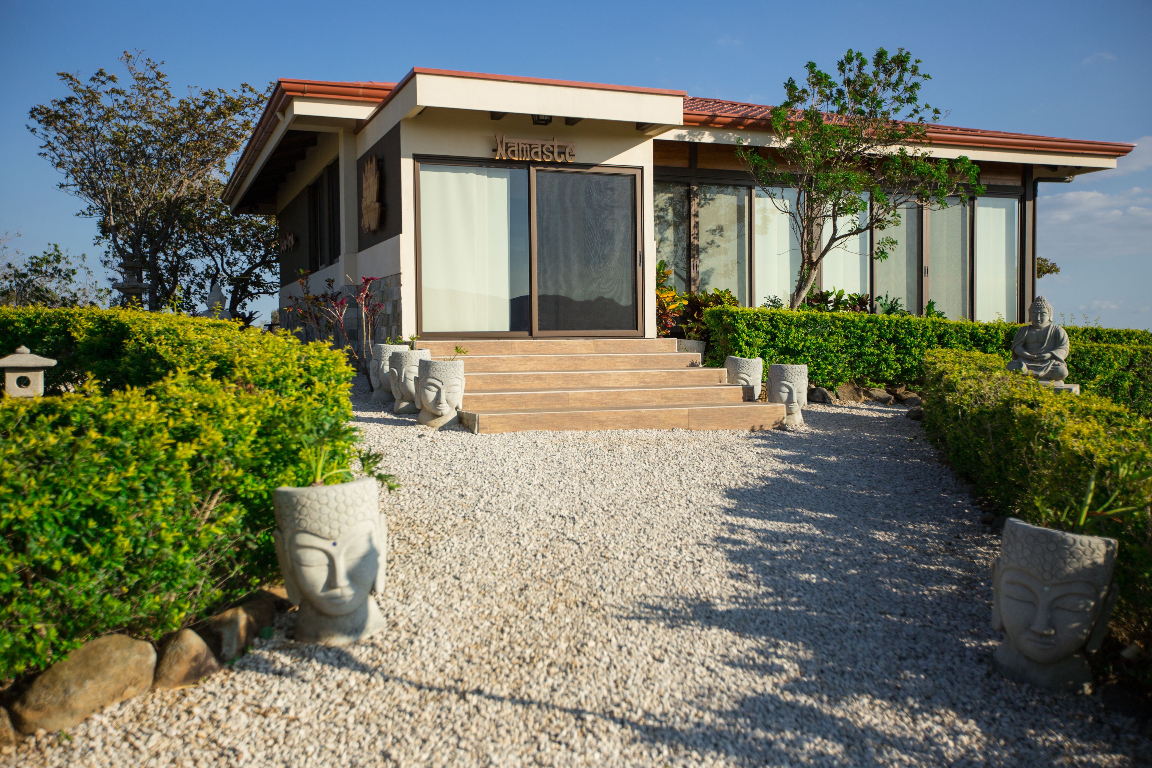 A modern building with a nameplate reading "Namaste," surrounded by well-maintained hedges and stone sculptures.