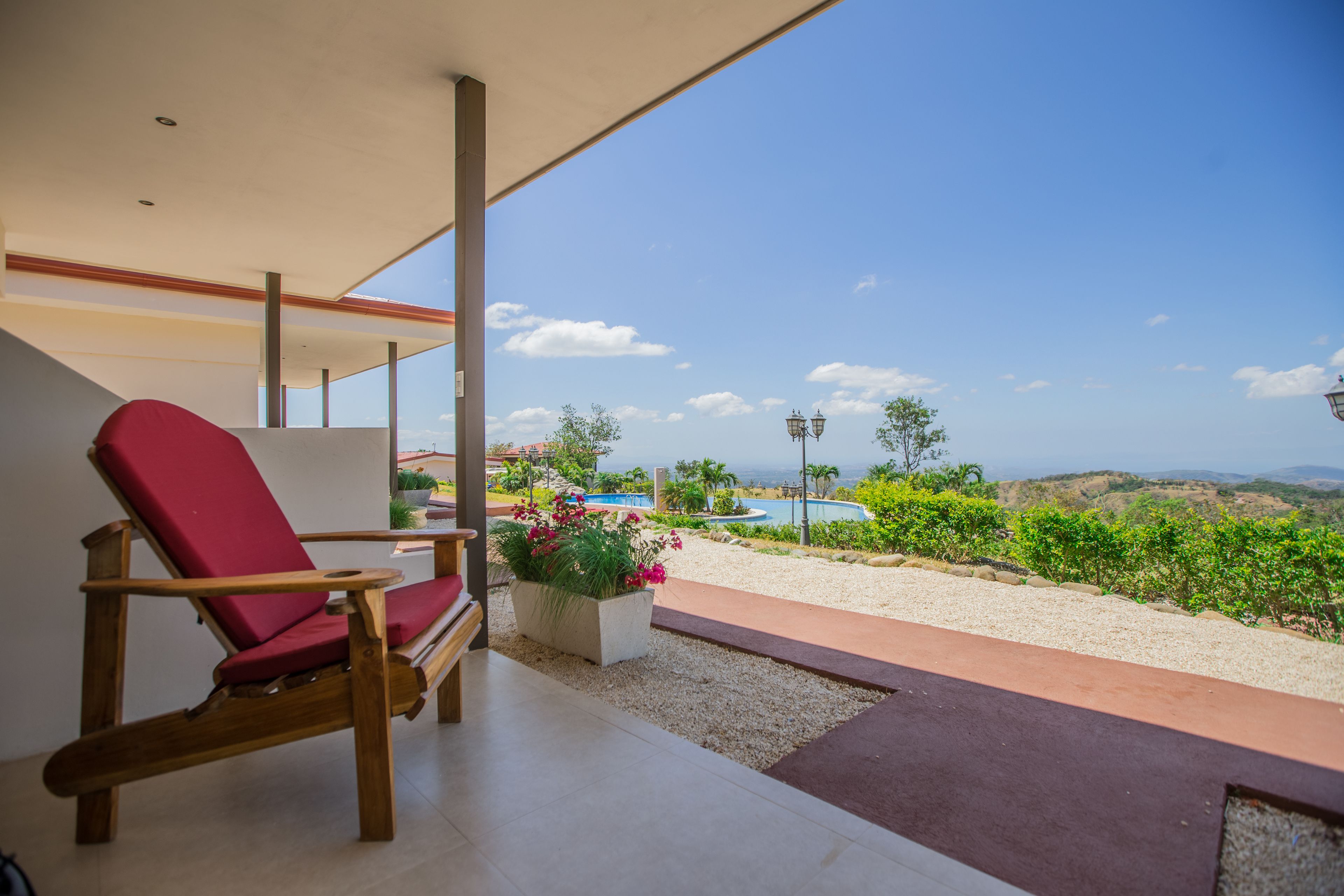 A modern outdoor seating area with a red chair and a planter with flowers, overlooking a pool and a scenic landscape.
