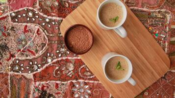 Two white cups of coffee on a wooden tray, placed on a patterned fabric.