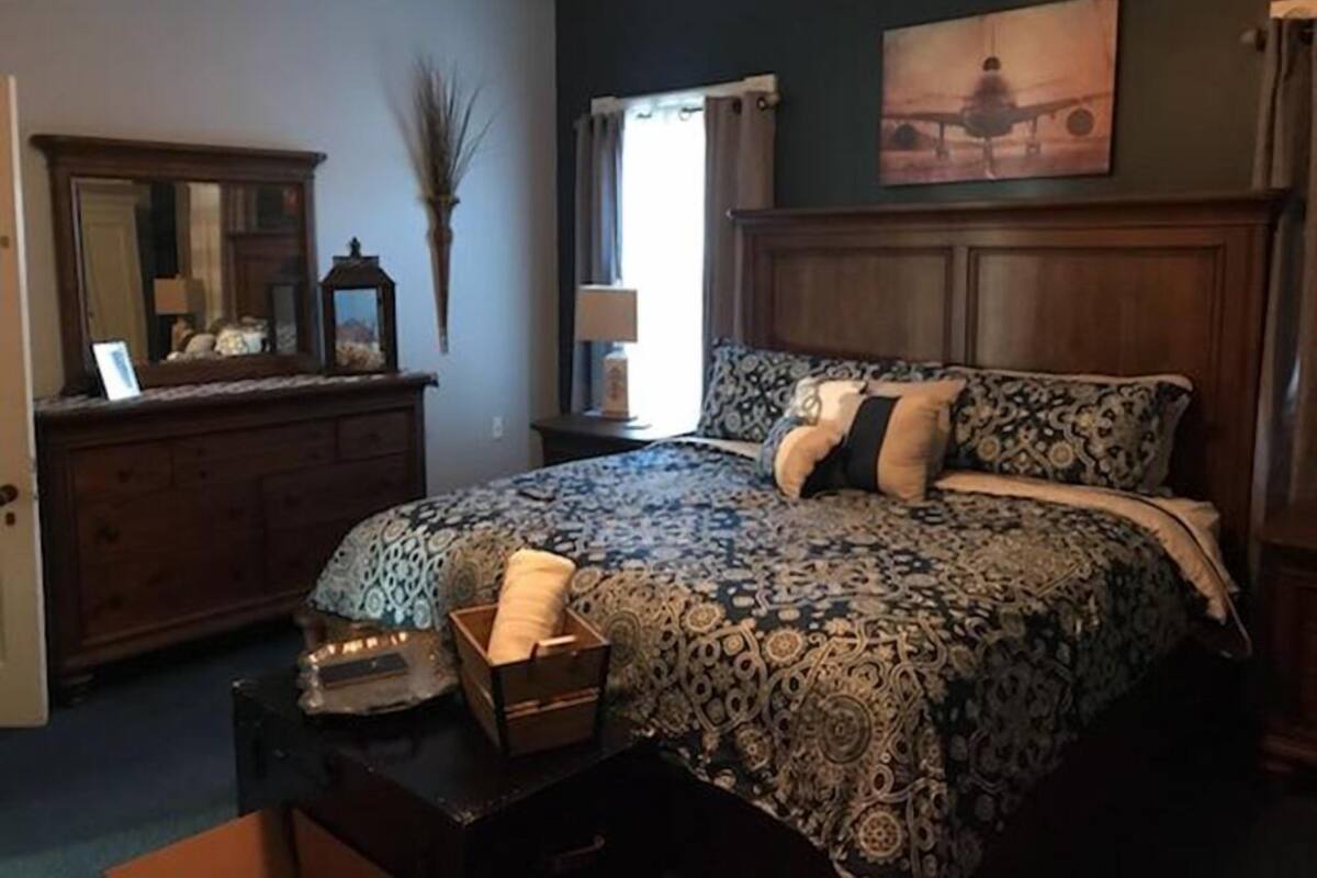A bedroom with a large bed, a dresser, a mirror, and a painting on the wall.