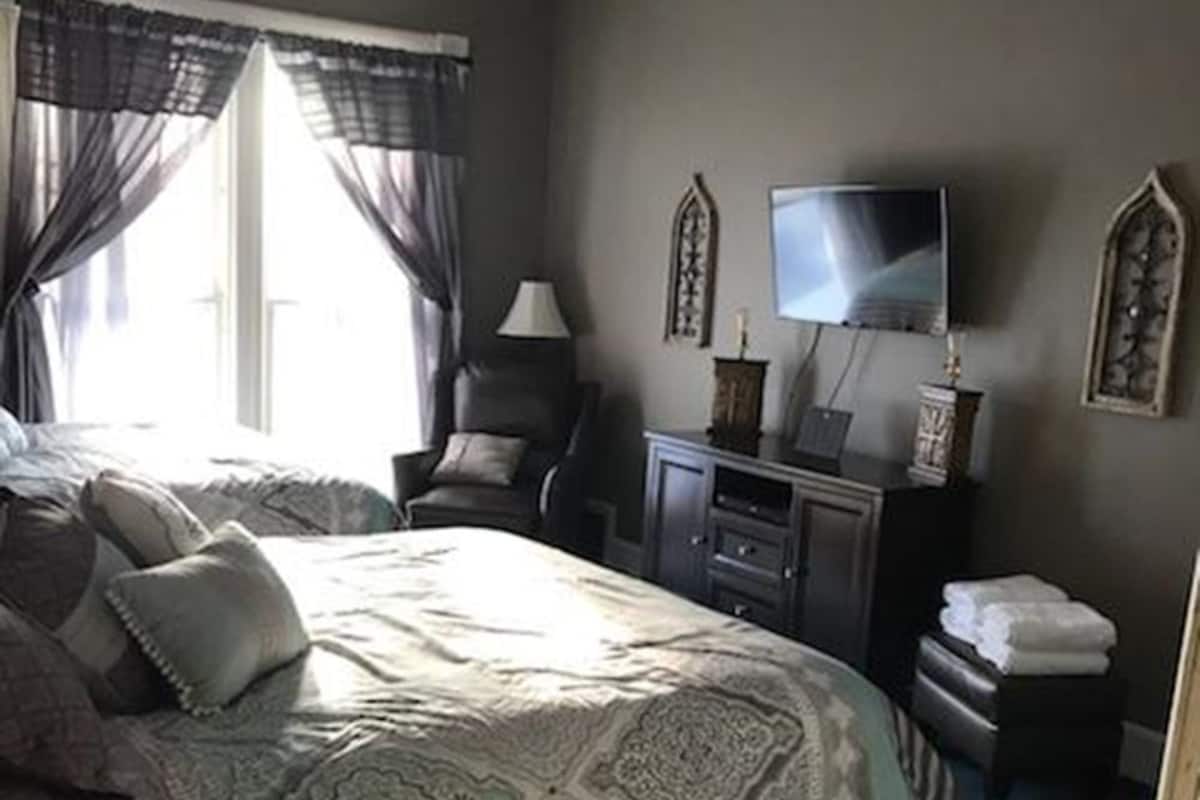 A bedroom with a bed, a desk, a chair, a television, and a ceiling fan.