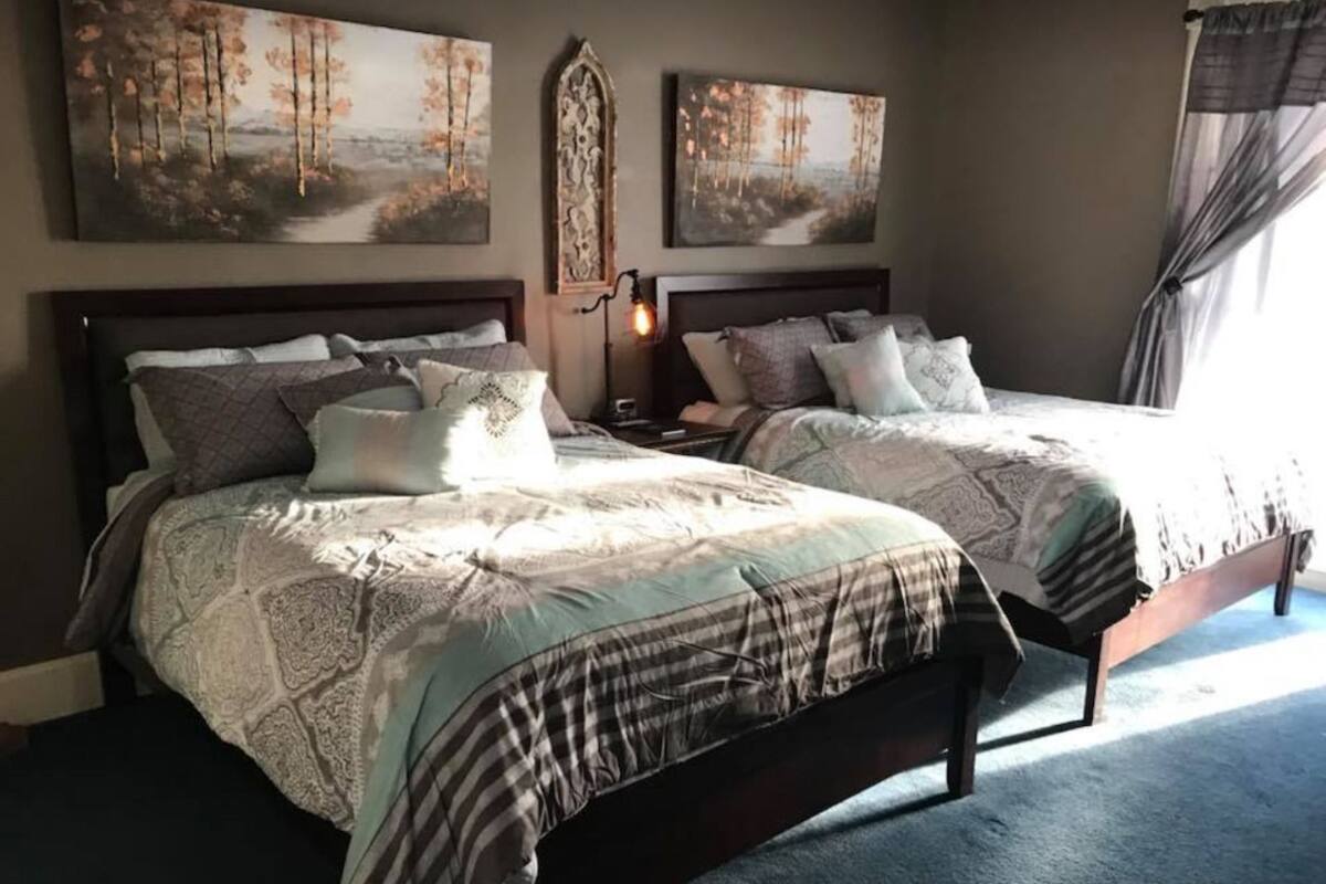 A bedroom with two beds, each with a headboard, a nightstand, and a wall-mounted lamp.