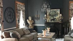 A living room with a dark wall, a chandelier, a fireplace, and a large clock. - Evans Holly Grove Inn B&B (Burlington)