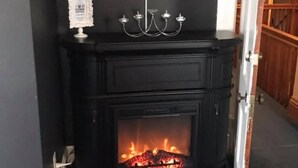 A black fireplace with a TV above it, a chandelier, and a door leading to another room. - Evans Holly Grove Inn B&B (Burlington)