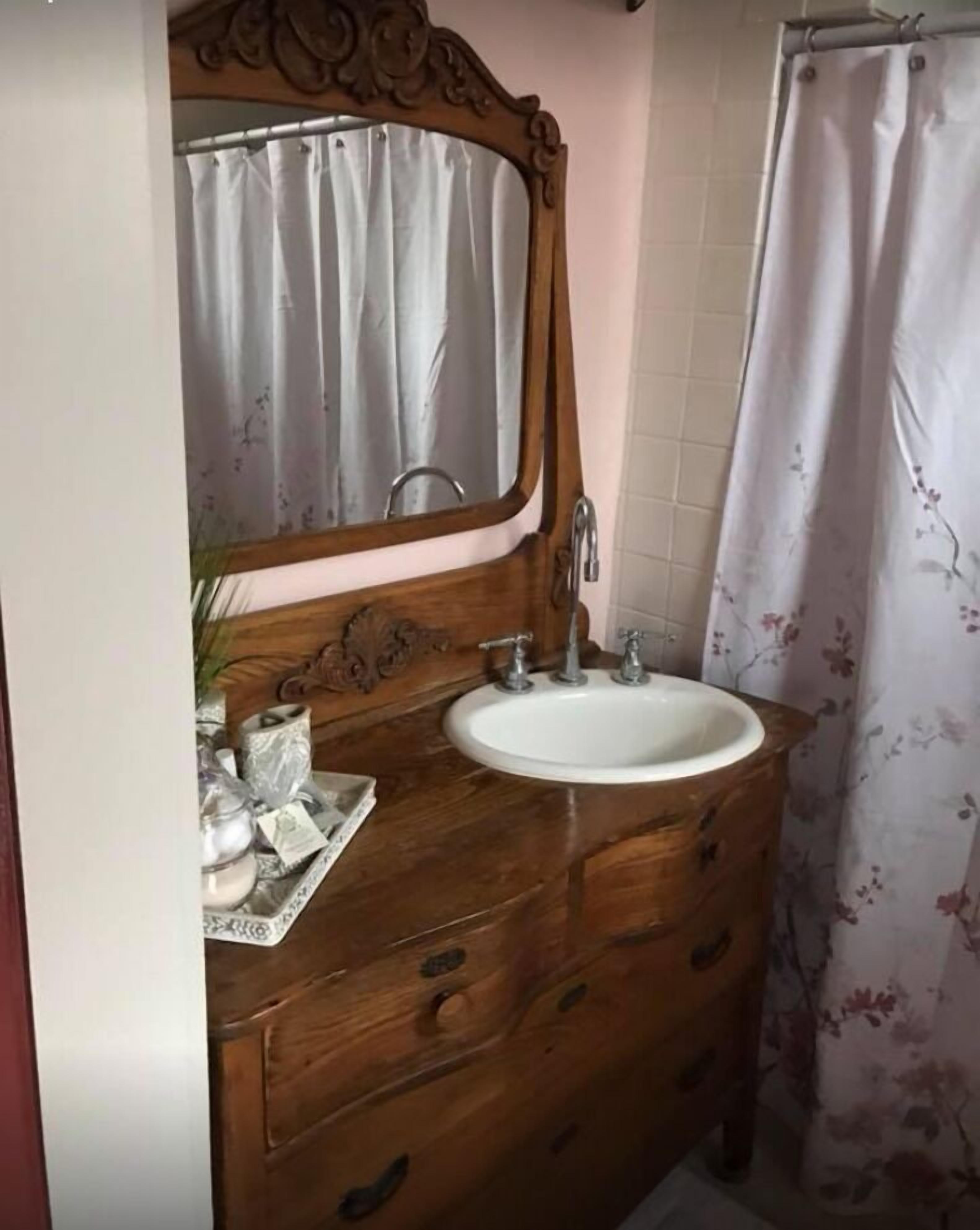 A bathroom with a wooden vanity, a white sink, and a mirror above it.