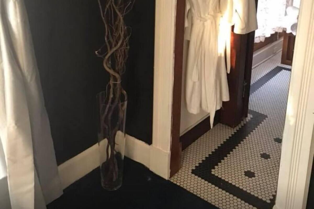 A hallway with a black wall, a white vase with branches, and two white robes hanging on a rack.