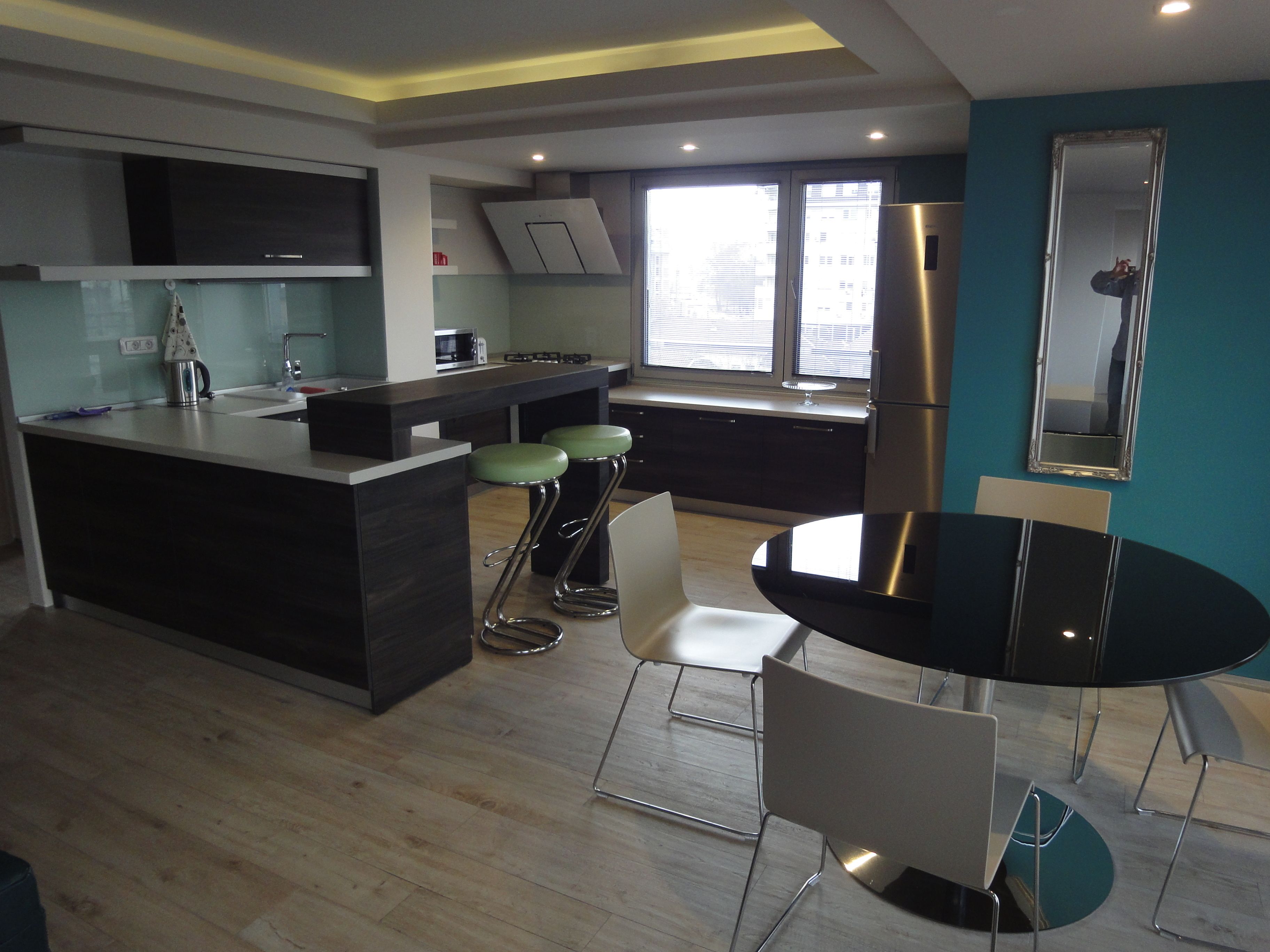 A modern kitchen with a central island, bar stools, a dining table, and a refrigerator.