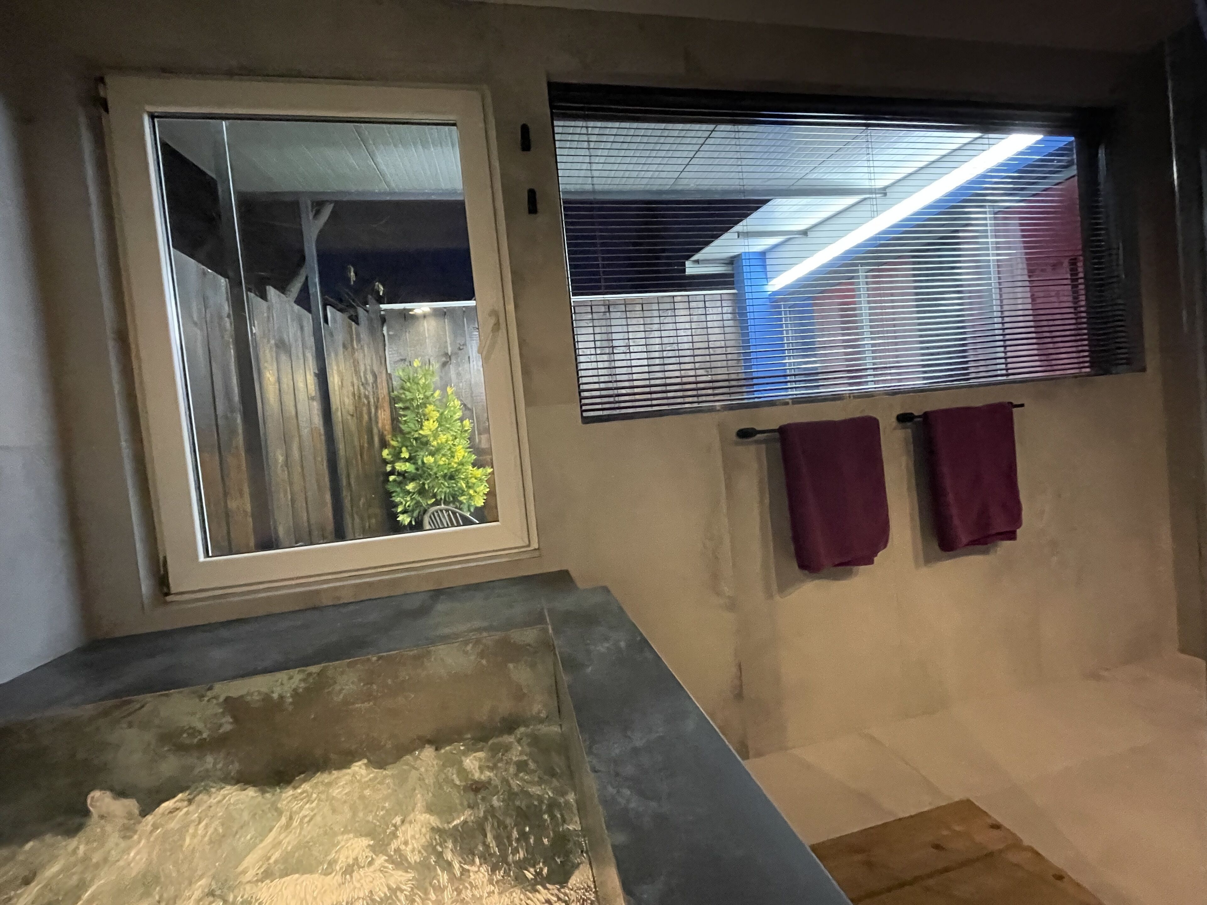 Une salle de bain avec une baignoire, une fenêtre avec des stores et un porte-serviettes avec deux serviettes.