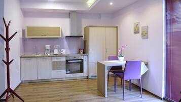 A modern kitchen with white cabinets, a built-in oven, and a dining area with a table and purple chairs.