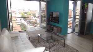 Un salon moderne avec un canapé blanc, une table basse en verre et un téléviseur fixé au mur.