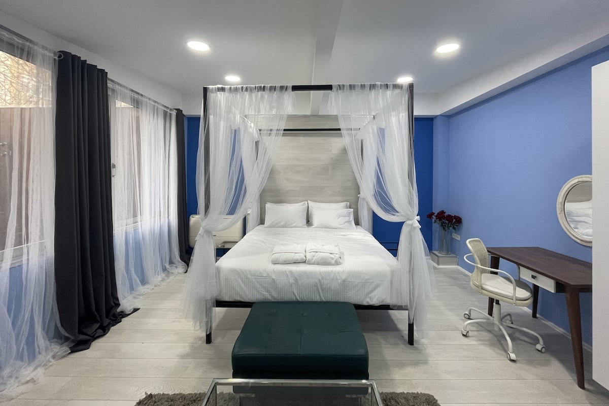 A modern hotel room with a four-poster bed, a desk, and a chair.
