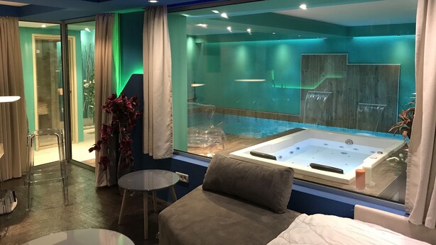 Une chambre d’hôtel moderne dotée d’une grande fenêtre, d’un jacuzzi, d’un canapé et d’une petite table.