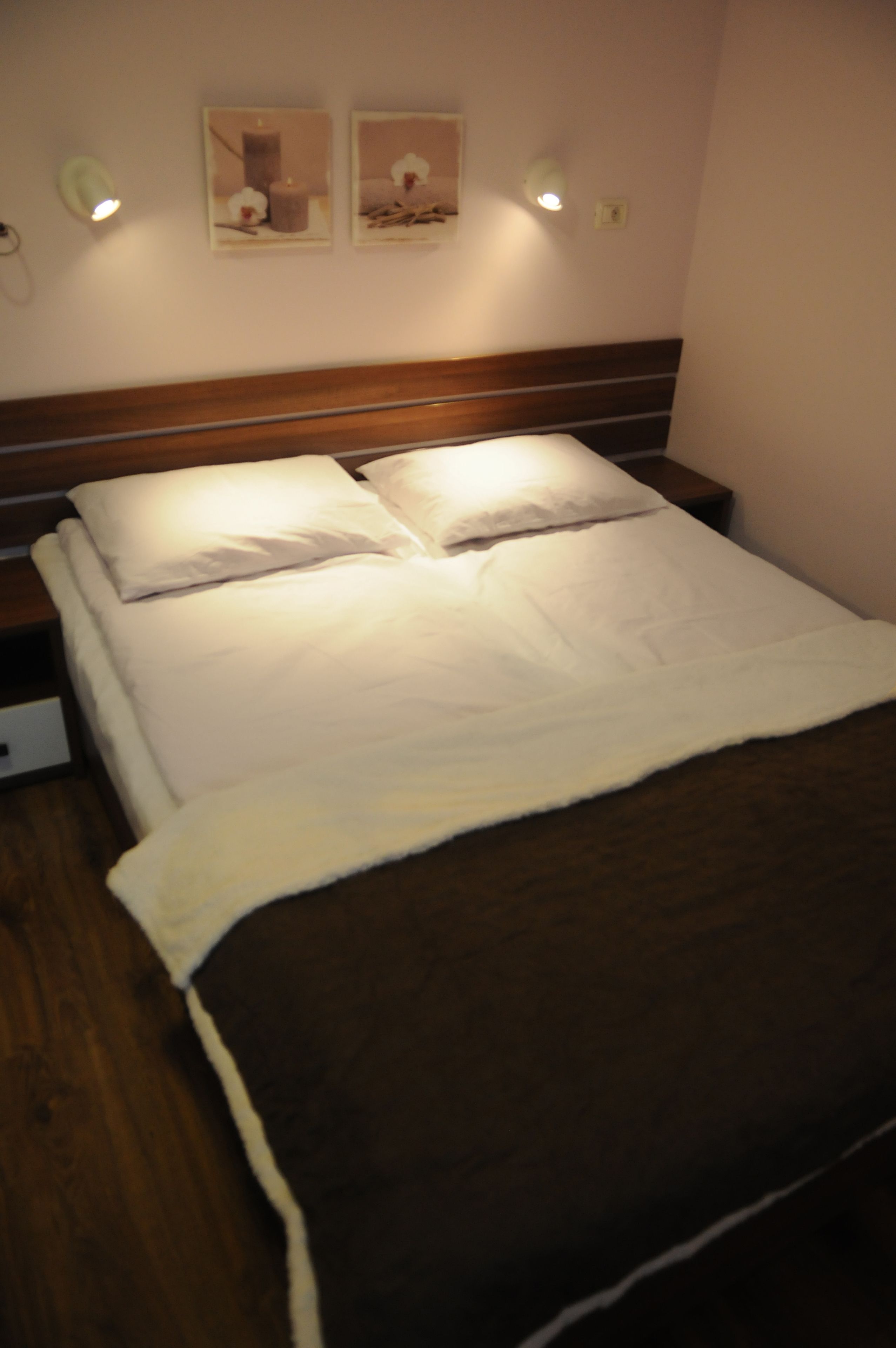 A neatly made bed with a wooden headboard, two bedside tables, and wall-mounted light fixtures.