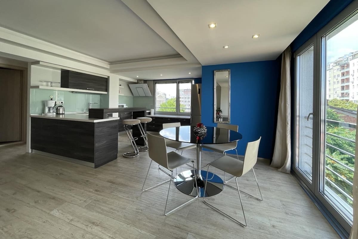 A modern kitchen with a central island, bar stools, and a dining table with chairs.