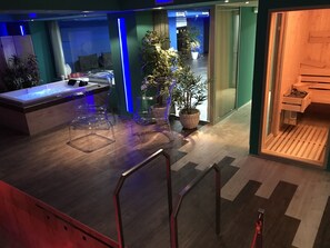 A modern hotel lobby with a reception desk, clear glass chairs, potted plants, and a wooden bench.