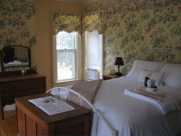 A bedroom with a bed, a desk, a chair, a dresser, a lamp, and a window with curtains. - Vintage Gardens Bed & Breakfast (Newark)