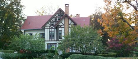 A Tudor-style house with a red-tiled roof, surrounded by lush greenery and autumn-colored trees.