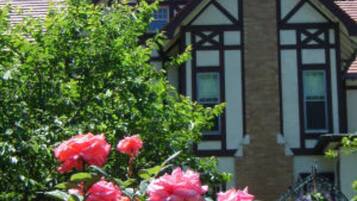 A Tudor-style house with a prominent chimney, large windows, and a well-maintained garden with pink roses.