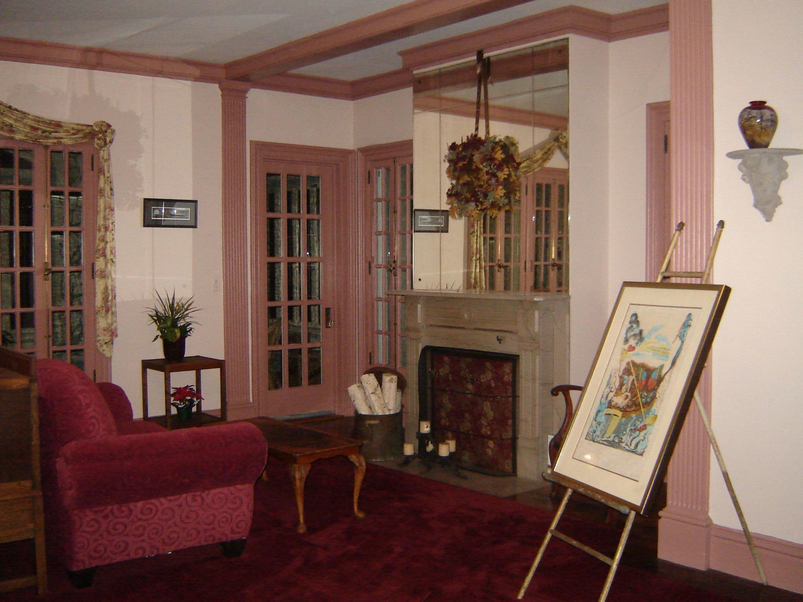 A room with a fireplace, a red armchair, a small table, and a painting on an easel.