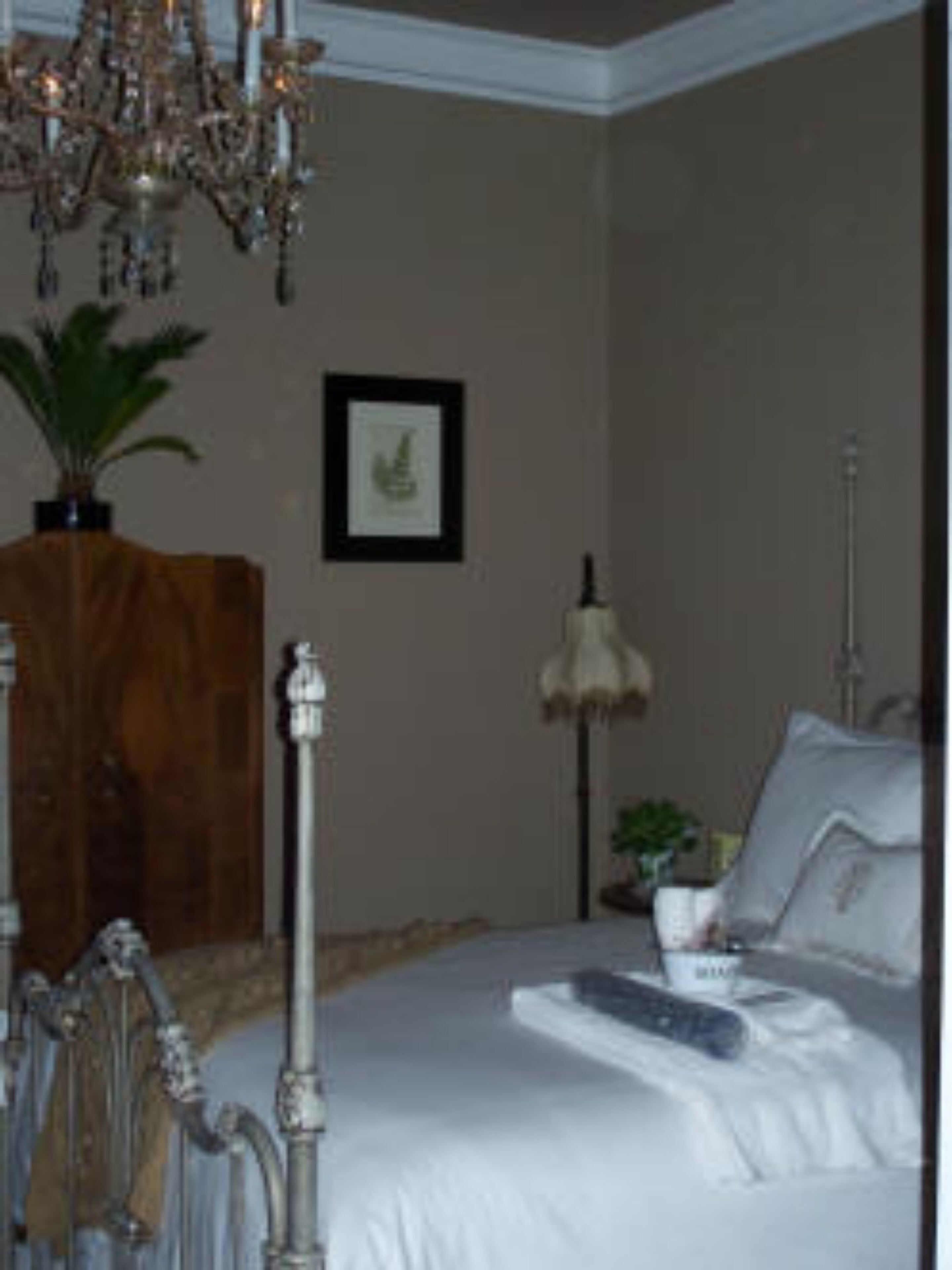A bedroom with a large bed, a chandelier, a wooden cabinet, a framed picture, and a lamp.